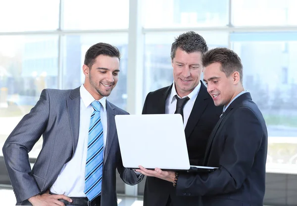 Geschäftskollegen blicken auf einen Laptop, der in der Lobby des Büros steht. — Stockfoto