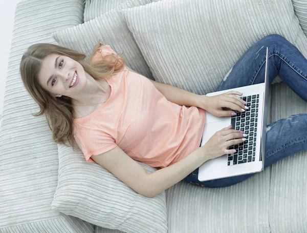 Дівчина студент працює з ноутбуком, сидячи на дивані і дивлячись на камеру . — стокове фото