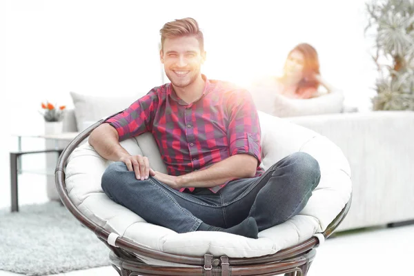 Jovem moderno sentado em uma grande cadeira redonda no fundo borrado — Fotografia de Stock