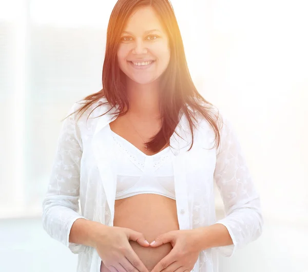 Mooie zwangere vrouw houdt handen in hart vorm op haar buik. — Stockfoto