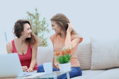 İki genç kadın kahve masasında konuşuyor ve oturuyor.