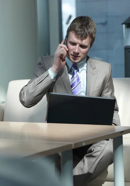 Aantrekkelijke Europese man praten over de telefoon terwijl het gebruiken van laptop. — Stockfoto