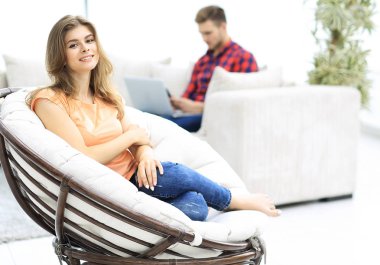 Güzel genç bir kadın büyük, rahat bir sandalyede oturuyor.