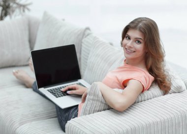 güzel genç kadın kanepede oturan ve kameraya bakarak dizüstü bilgisayar ile çalışma.