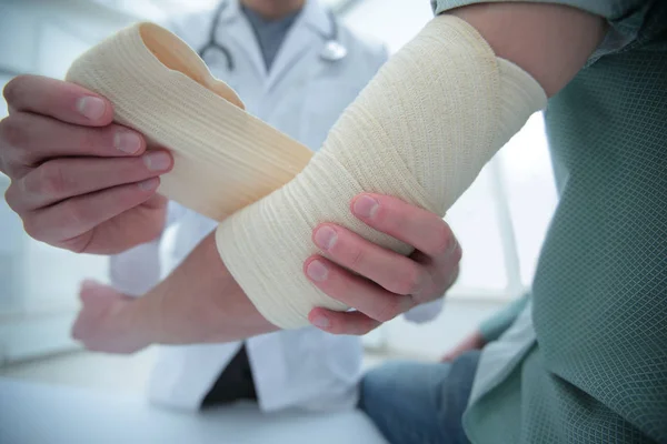 Orthopédiste appliquant un bandage sur les patients main dans la main en clinique — Photo