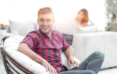 Bulanık arka planda büyük bir sandalyede oturan mutlu genç adam.