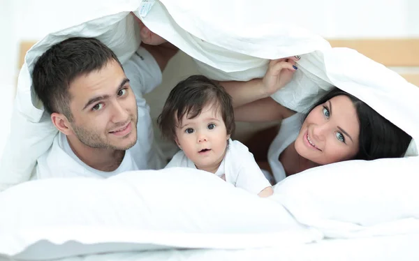 Família feliz posando sob um edredom enquanto olha para a câmera — Fotografia de Stock