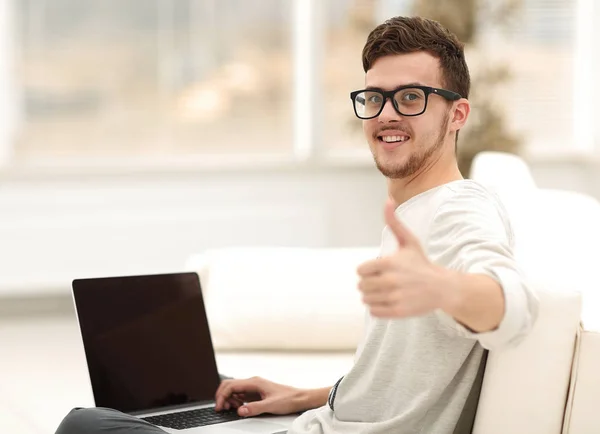 Современный молодой человек сидит перед открытым ноутбуком и показывает большой палец вверх — стоковое фото