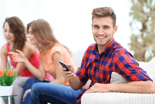 Tipo moderno con un teléfono inteligente y sus amigos sentados en el sofá — Foto de Stock