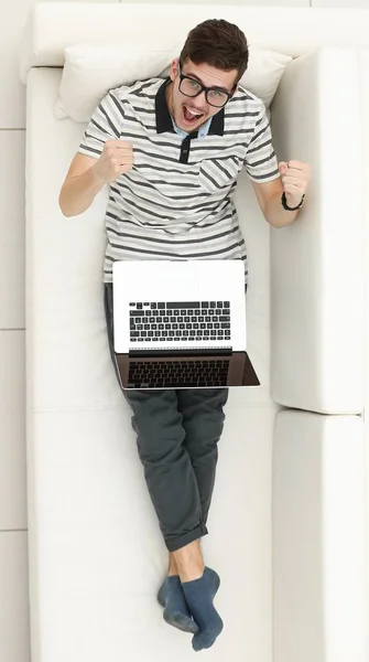 Homem moderno feliz olha para o laptop sentado no sofá . — Fotografia de Stock