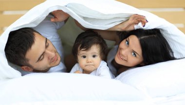 mutlu bir aile kameraya bakarken bir yorgan altında poz