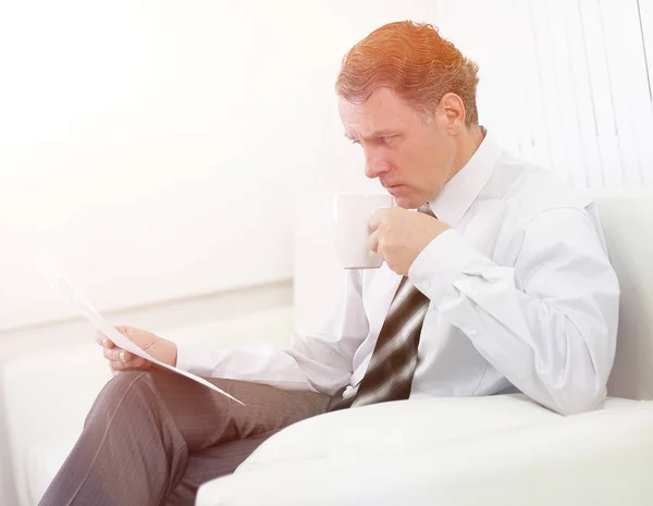 Geschäftsmann liest ein Dokument, während er im Hotelzimmer auf einem Stuhl sitzt. — Stockfoto