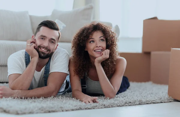 Casal jovem deitado no tapete no fundo de um novo apartamento — Fotografia de Stock