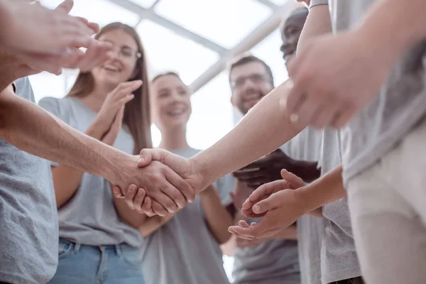 Handshake of young people on the background of the applauding team — Stock Photo, Image