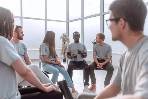 Jeune homme souriant assis dans un cercle de personnes partageant les mêmes idées — Photo