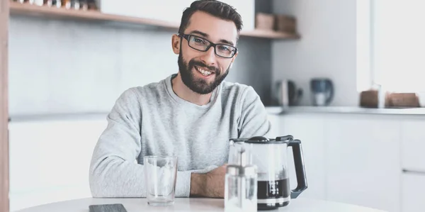 Atractivo hombre sentado en la mesa de la cocina por la mañana — Foto de Stock