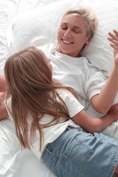 Mãe feliz falando com sua filha deitada na cama . — Fotografia de Stock