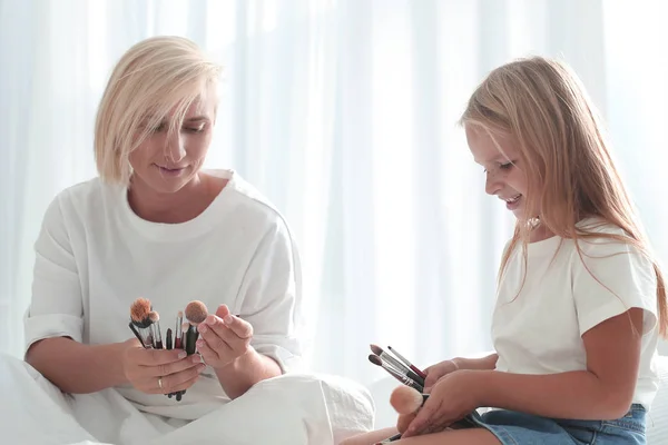 Madre con hija pequeña mirando el cepillo de maquillaje . — Foto de Stock
