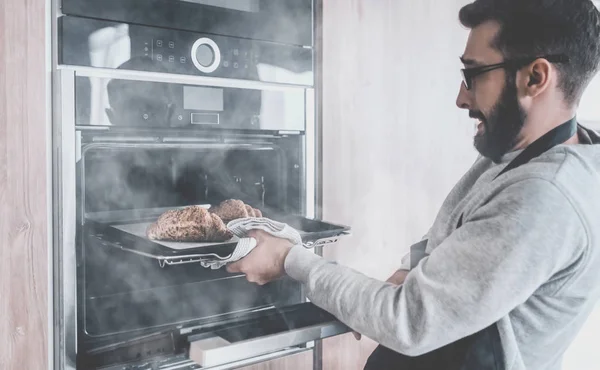 De cerca. un joven saca de la bandeja del horno de croissants — Foto de Stock