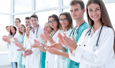 Sıraya dizilmiş gülümseyen genç doktorlar alkışlıyor.