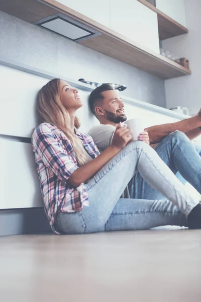 Pareja joven tomando café sentado en el suelo de la cocina — Foto de Stock