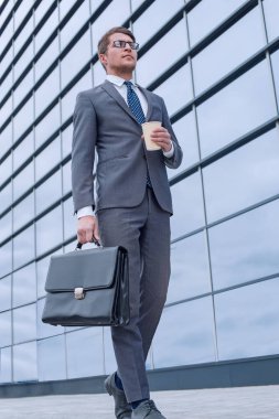 İş adamı elinde kahve ile iş merkezinin yanında yürüyor.