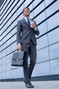 İş adamı elinde kahve ile iş merkezinin yanında yürüyor.