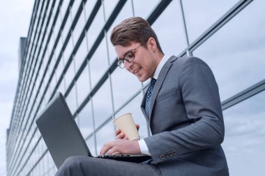 Kahveli bir iş adamı ofis binasının yanında dizüstü bilgisayar kullanıyor.