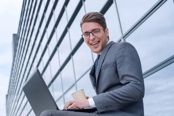 Kahveli bir iş adamı ofis binasının yanında dizüstü bilgisayar kullanıyor.