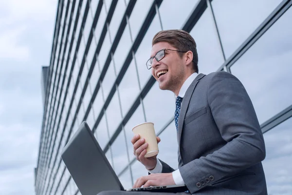 Homme d'affaires avec un café à emporter utilise un ordinateur portable près d'un immeuble de bureaux — Photo
