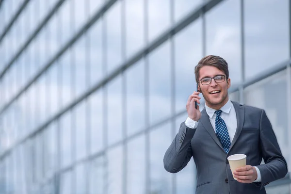 young businessman with coffee talking on smartphone