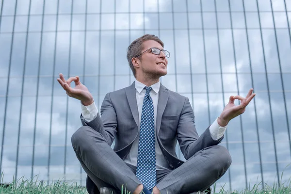 Homme d'affaires à Lotus pose assis sur l'herbe en face de l'immeuble de bureaux — Photo