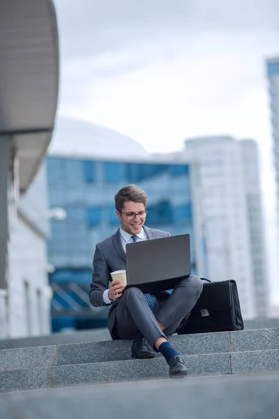 Homem de negócios usando seu laptop sentado nos degraus em uma rua da cidade — Fotografia de Stock