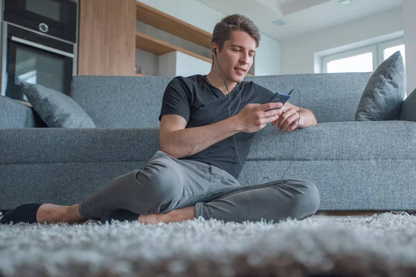 Avslappnad ung man sitter på golvet i sitt vardagsrum — Stockfoto