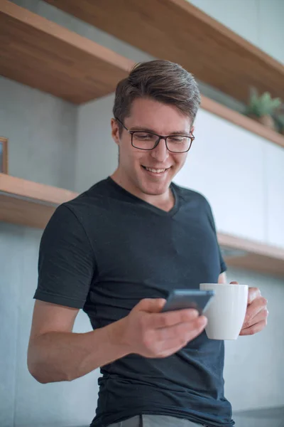 Hombre joven casual usando teléfono inteligente en la cocina —  Fotos de Stock