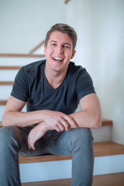 Neşeli genç adam evinin merdivenlerinde oturuyor.