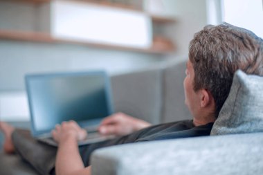 Dizüstü bilgisayarı olan genç adam rahat koltukta yatıyor.