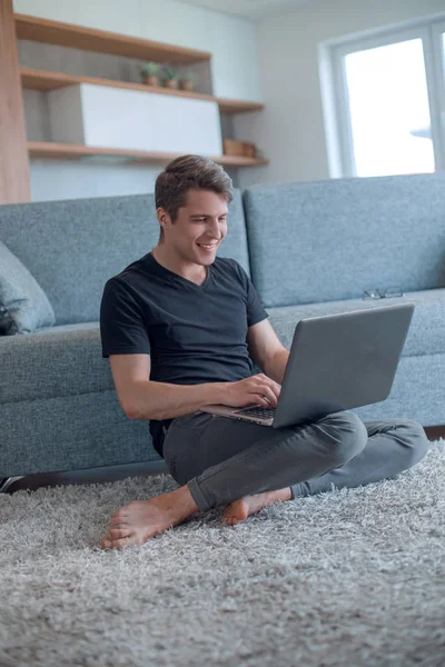 Νεαρός άνδρας πληκτρολογώντας στο laptop του στο άνετο σαλόνι — Φωτογραφία Αρχείου