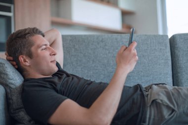 Genç adam kanepede uzanmış yazışmaları okuyor.