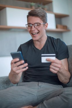 Banka kartlı gülümseyen adam koltukta oturuyor.