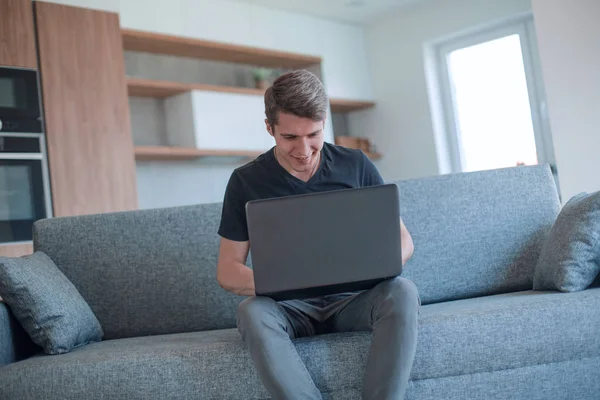 Ernsthafter junger Mann arbeitet in seiner Wohnung an einem Laptop — Stockfoto