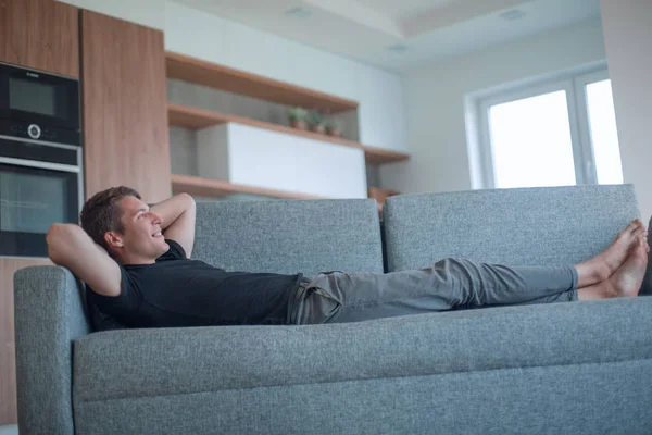Felice giovane uomo sdraiato sul divano in accogliente soggiorno — Foto Stock