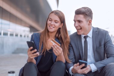 Banka kartı kullanan genç çift ofis binasının yanında oturuyor.