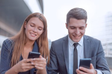 Akıllı telefonları olan iki genç çalışan ofis binasının yanında oturuyor.