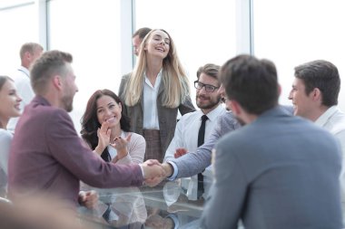 Gülümseyen iş ortakları iş dünyasının alkışlarıyla el sıkışıyor.