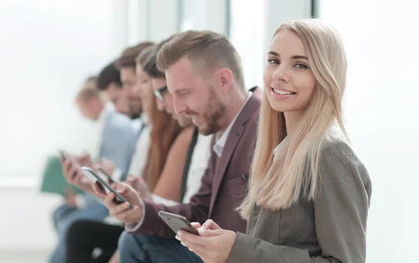 Jóvenes empresarios con smartphones sentados en el pasillo de oficinas . — Foto de Stock