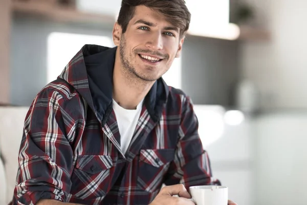 Joven con una taza de café en el fondo en la cocina —  Fotos de Stock