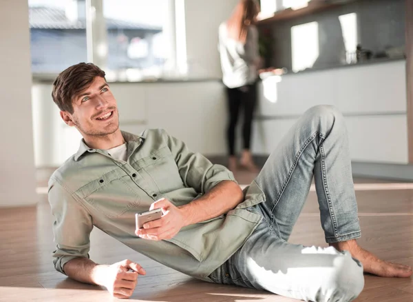 Młody człowiek ze smartfonem siedzi na podłodze w kuchni — Zdjęcie stockowe