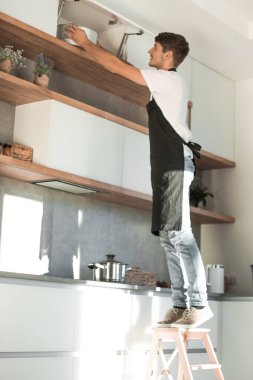 ev mutfağında bir merdiven üzerinde duran adam