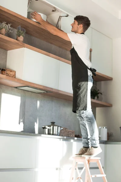 Hombre de pie sobre una escalera en la cocina del hogar — Foto de Stock